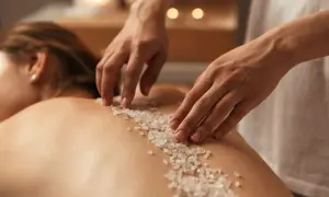 Mani esperte applicano un scrub corpo con cristalli di sale sulla schiena di una persona, un rituale di benessere prima della doccia.