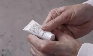 Mani che stringono un tubetto di crema, forse un trattamento iodase anticellulite tiroide, leggendo attentamente gli ingredienti.