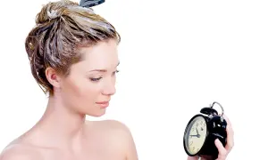 Donna con capelli trattati con maschera, osserva un orologio. Impara come si usa la maschera per capelli per un trattamento efficace.