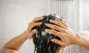 Mani che massaggiano shampoo sui capelli scuri sotto la doccia. Lavare i capelli tutti i giorni fa male, meglio farlo meno spesso.