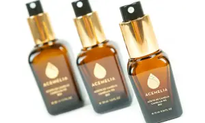 Tre flaconi di olio di camelia per capelli, con tappo dorato e spruzzino nero, su sfondo bianco.