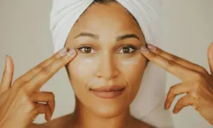 Donna con turbante applica crema contorno occhi, mostrando la differenza tra unguento e crema per la cura della pelle.