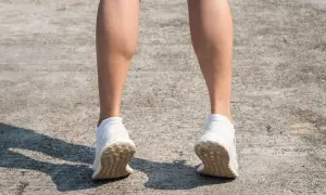 Gambe di donna con polpacci grossi, forse a causa di allenamento intenso. Scarpe da ginnastica bianche su cemento.