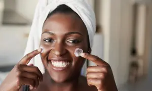 Donna sorridente con turbante applica crema sul viso, un'immagine che evoca il desiderio di vedere i risultati del **retinolo prima e dopo**.