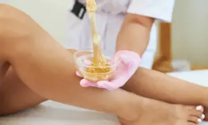 Una mano con guanto rosa preleva cera da una ciotola per la depilazione femminile delle gambe.