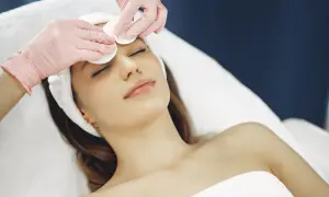 Mani con guanti rosa eseguono una delicata pulizia del viso con dischetti di cotone su una donna rilassata.