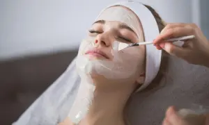 Una donna riceve un peeling viso. La maschera bianca viene applicata con un pennello, mostrando come si fa un trattamento di bellezza.