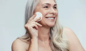 Donna sorridente con cotone per la pulizia del viso, mostrando la differenza tra latte detergente e detergente viso.