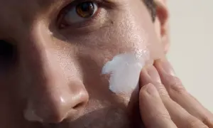 Primo piano di un uomo che applica crema sul viso. La cura della pelle per la pulizia viso uomo è un gesto di benessere.