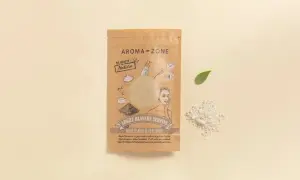 Confezione di maschera argilla bianca Aroma-Zone, con polvere sparsa e fogliolina verde su sfondo chiaro.