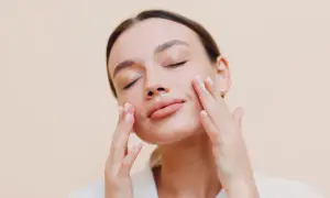 Donna con occhi chiusi applica delicatamente una crema sebo regolatrice sul viso, godendosi un momento di cura della pelle.