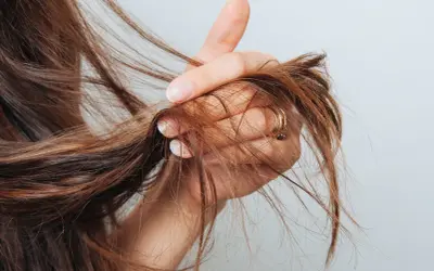 Mano che mostra capelli con doppie punte, un segno di capelli secchi e danneggiati che necessitano di cure.