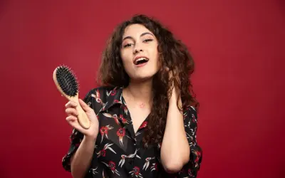 Ragazza con capelli ricci pettinati, tiene in mano una spazzola per capelli.