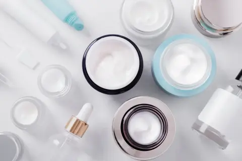 Varietà di creme e flaconi per la cura della pelle. Alcuni contenitori sono aperti, mostrando la texture cremosa. Non è dmae vietato l'uso di questi prodotti.
