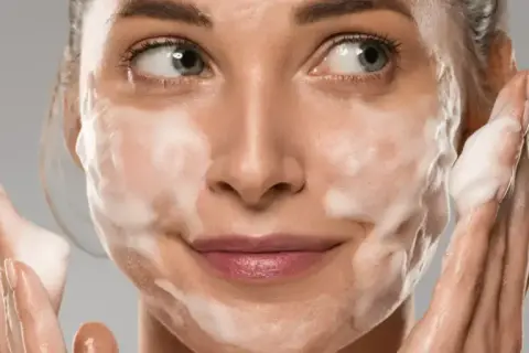 Donna con schiuma sul viso, che mostra come si usa il detergente viso per una pulizia profonda e delicata.
