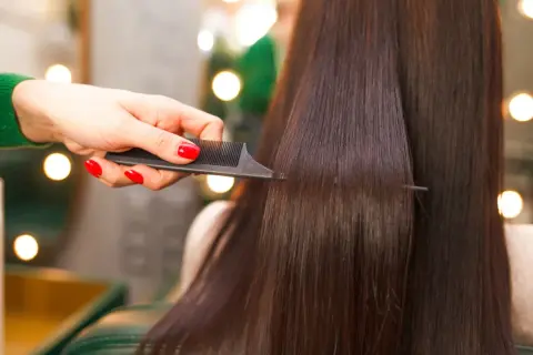 Mano con unghie rosse pettina capelli lisci e scuri, creando un look impeccabile.