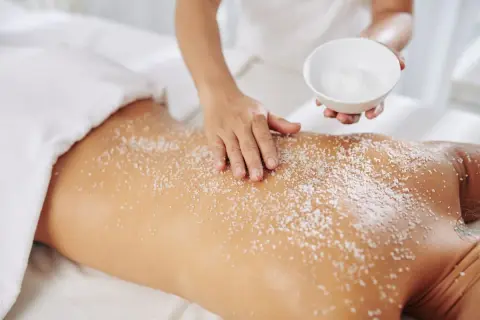 Mani esperte applicano un massaggio scrub con sale sulla schiena di una persona, per un'esfoliazione profonda e rigenerante.