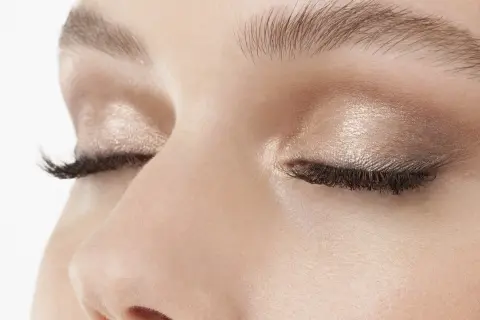 Occhi chiusi con trucco luminoso, ciglia lunghe e folte. Uno sguardo spento che riflette un momento di quiete interiore.