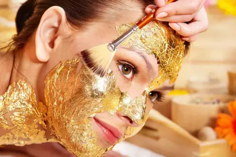 Una donna riceve un trattamento di bellezza con una maschera viso oro, scoprendo i suoi benefici rigeneranti.