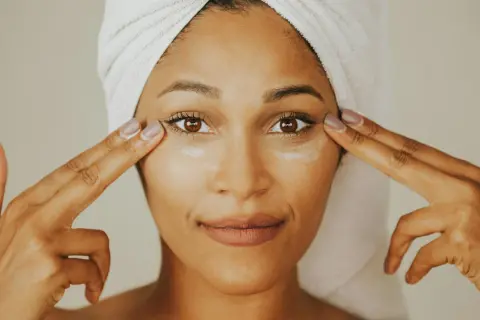 Donna con turbante applica crema contorno occhi, mostrando la differenza tra unguento e crema per la cura della pelle.