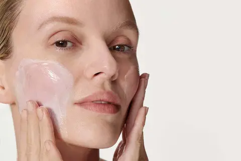 Donna applica una crema idratante sul viso. La sua pelle appare luminosa e sana, pronta per il giorno. Prima scrub o detergente? La scelta è tua per una pelle perfetta.