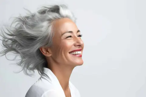 Donna sorridente con splendidi capelli bianchi mossi dal vento.