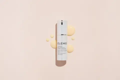 Siero ELEMIS con acido glicolico e vitamina C, per una pelle luminosa e rinnovata, circondato da gocce dorate.