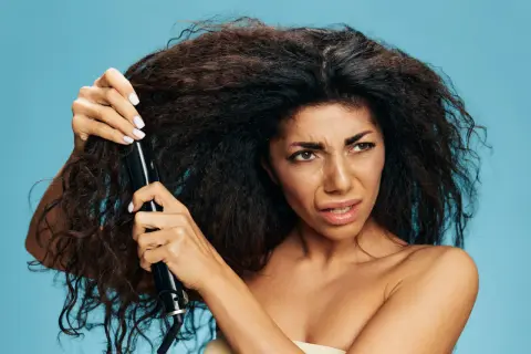 Donna con capelli crespi prova a usare una piastra, sperando in un trattamento anti crespo efficace.