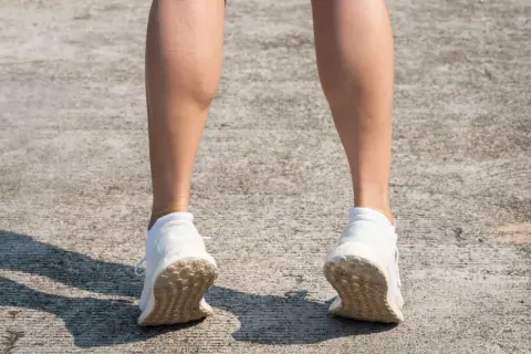 Gambe di donna con polpacci grossi, forse a causa di allenamento intenso. Scarpe da ginnastica bianche su cemento.