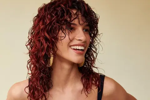 Donna sorridente con splendidi capelli mogano ricci e bagnati, che le incorniciano il viso.