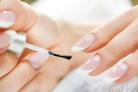 Mani perfette con la manicure a casa. Smalto trasparente applicato con cura su unghie con french manicure.