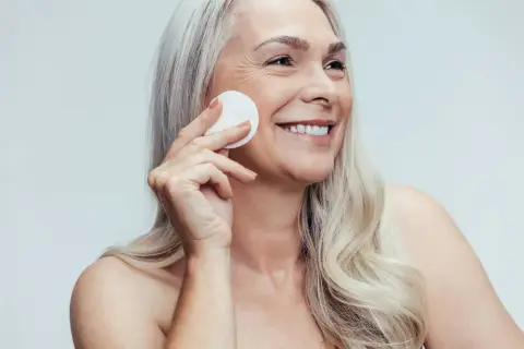Donna sorridente con cotone per la pulizia del viso, mostrando la differenza tra latte detergente e detergente viso.