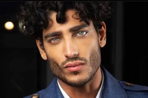 Uomo con capelli mossi scuri e occhi azzurri penetranti, un look che ispira su come farsi i capelli mossi uomo.
