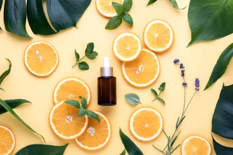 Siero viso con niacinamide e vitamina c, circondato da fette d'arancia, foglie verdi e lavanda.