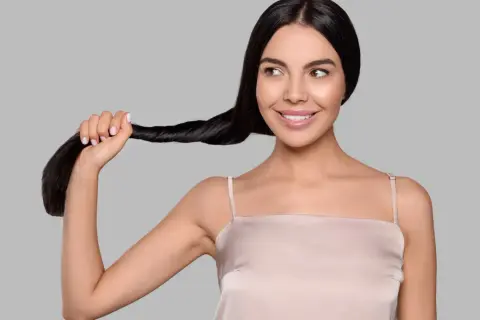 Una donna sorride mentre tiene una ciocca dei suoi lunghi capelli neri. Sembra che si chieda: "henne cos'è?