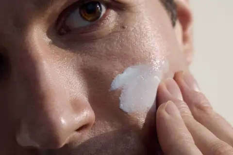 Primo piano di un uomo che applica crema sul viso. La cura della pelle per la pulizia viso uomo è un gesto di benessere.