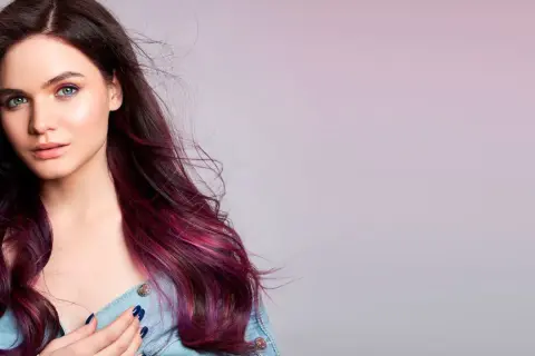 Modella con capelli viola prugna scuro che sfumano in tonalità più chiare, occhi verdi e trucco audace.
