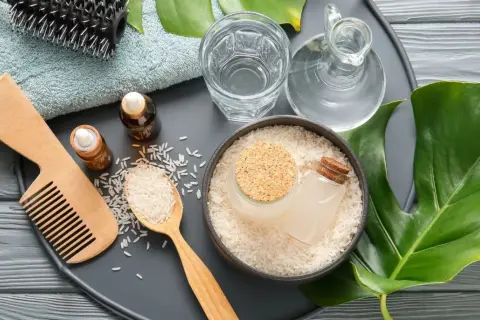 Ingredienti naturali per la cura dei capelli: riso, acqua, oli essenziali, pettine e spazzola. L'acqua di riso capelli è un segreto di bellezza.