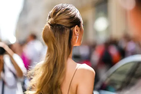 Capelli lunghi e ondulati, di un caldo biondo miele, raccolti in una coda bassa. Orecchini luminosi completano il look.