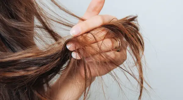 Mano che mostra capelli con doppie punte, un segno di capelli secchi e danneggiati che necessitano di cure.