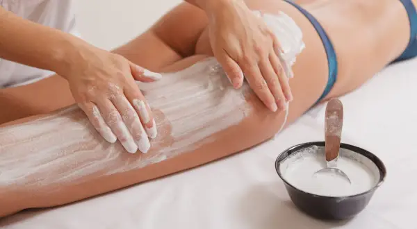 Mani esperte applicano fanghi drenanti su gambe e glutei, un trattamento che promette di aiutare a dimagrire e rimodellare il corpo.