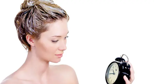 Donna con capelli trattati con maschera, osserva un orologio. Impara come si usa la maschera per capelli per un trattamento efficace.
