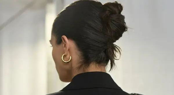 Capelli raccolti in uno chignon elegante, con un look effetto bagnato che dona lucentezza. Orecchino a cerchio dorato.