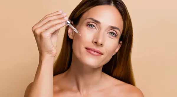 Donna applica un siero sul viso con un contagocce, un gesto essenziale per sapere come esfoliare la pelle e mantenerla luminosa.
