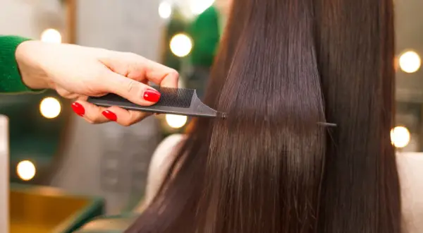 Mano con unghie rosse pettina capelli lisci e scuri, creando un look impeccabile.