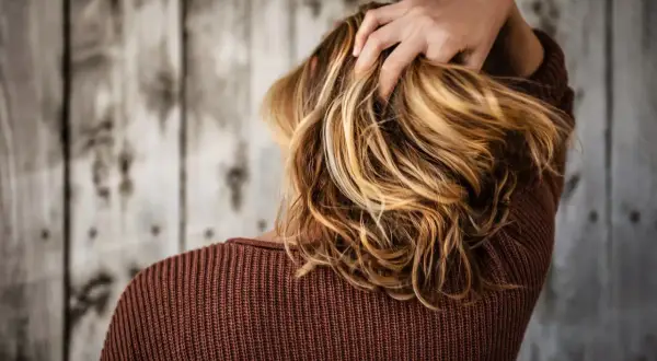 Capelli biondi mossi, una mano li accarezza. La vitamina C capelli dona lucentezza e forza.