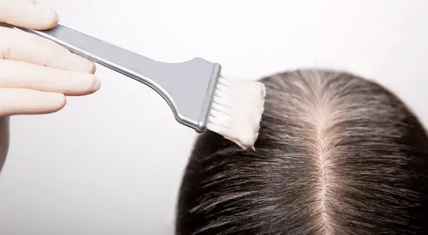 Guanto e pennello applicano tinta sui capelli scuri, mostrando come fare la tinta in casa per un cambio look.