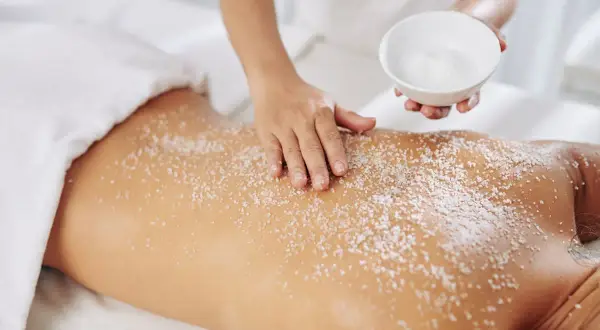 Mani esperte applicano un massaggio scrub con sale sulla schiena di una persona, per un'esfoliazione profonda e rigenerante.