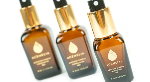 Tre flaconi di olio di camelia per capelli, con tappo dorato e spruzzino nero, su sfondo bianco.