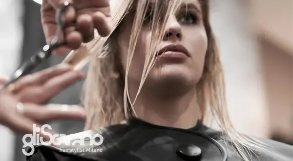 Un parrucchiere taglia i capelli biondi di una modella. La domanda "ogni quanto tagliare i capelli" è fondamentale per mantenere la chioma sana.
